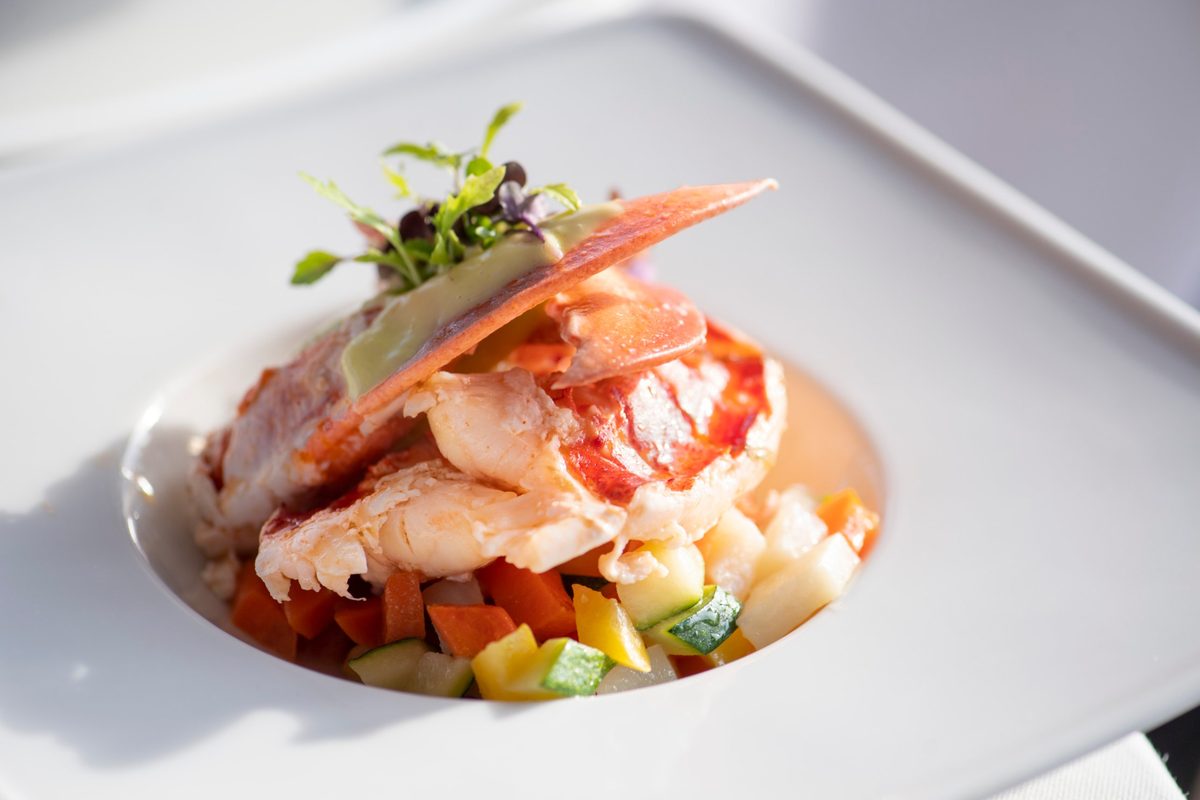 A plated lobster dish over diced vegetables, topped with microgreens