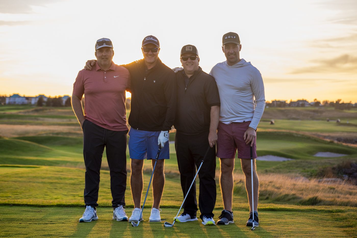 Four golfers standing together on a tee at sunset, the course behind them