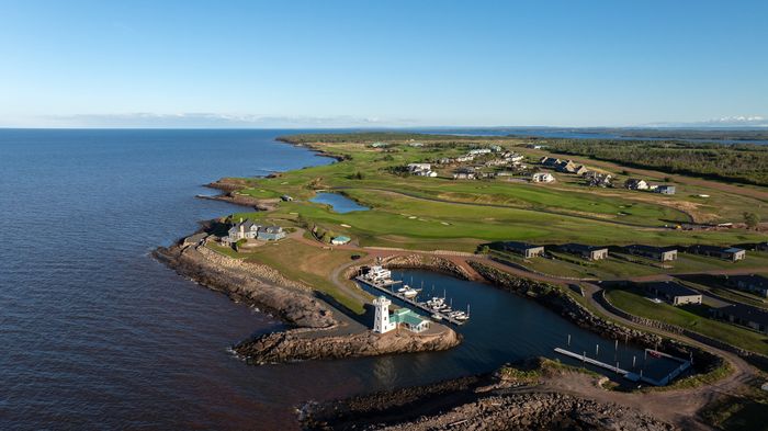 Aerial view of the Fox Harb'r marina and lighthouse, with boats at the docks and the golf course along the shore