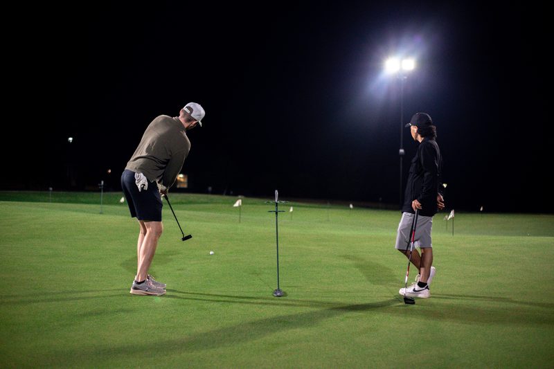 Two golfers putting at night on The Strait putting course under floodlights