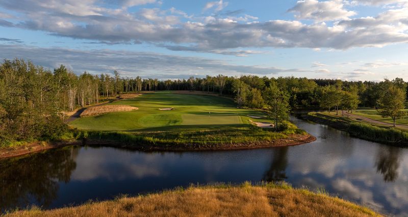 The 8th green on the Vineyard Course, wrapped by a pond and trees in warm evening light